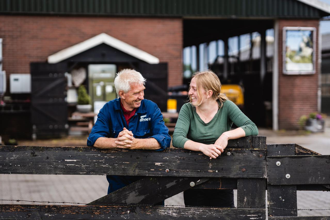 Vader en dochter staan te overleggen leunend op hek op boerderij