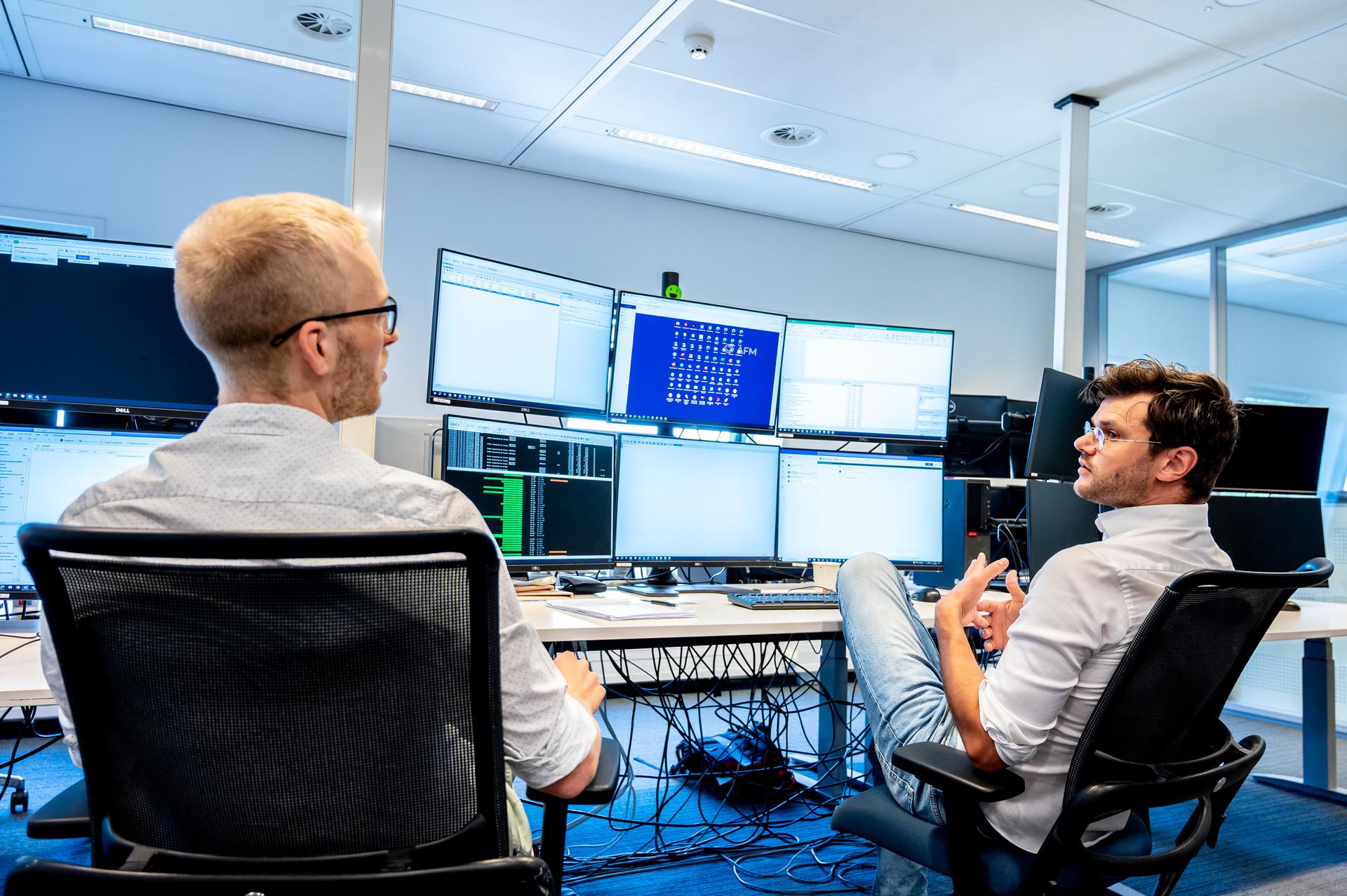 Twee mannelijke collega's in overleg, kijkend op een beeldscherm, in de Monitoringroom