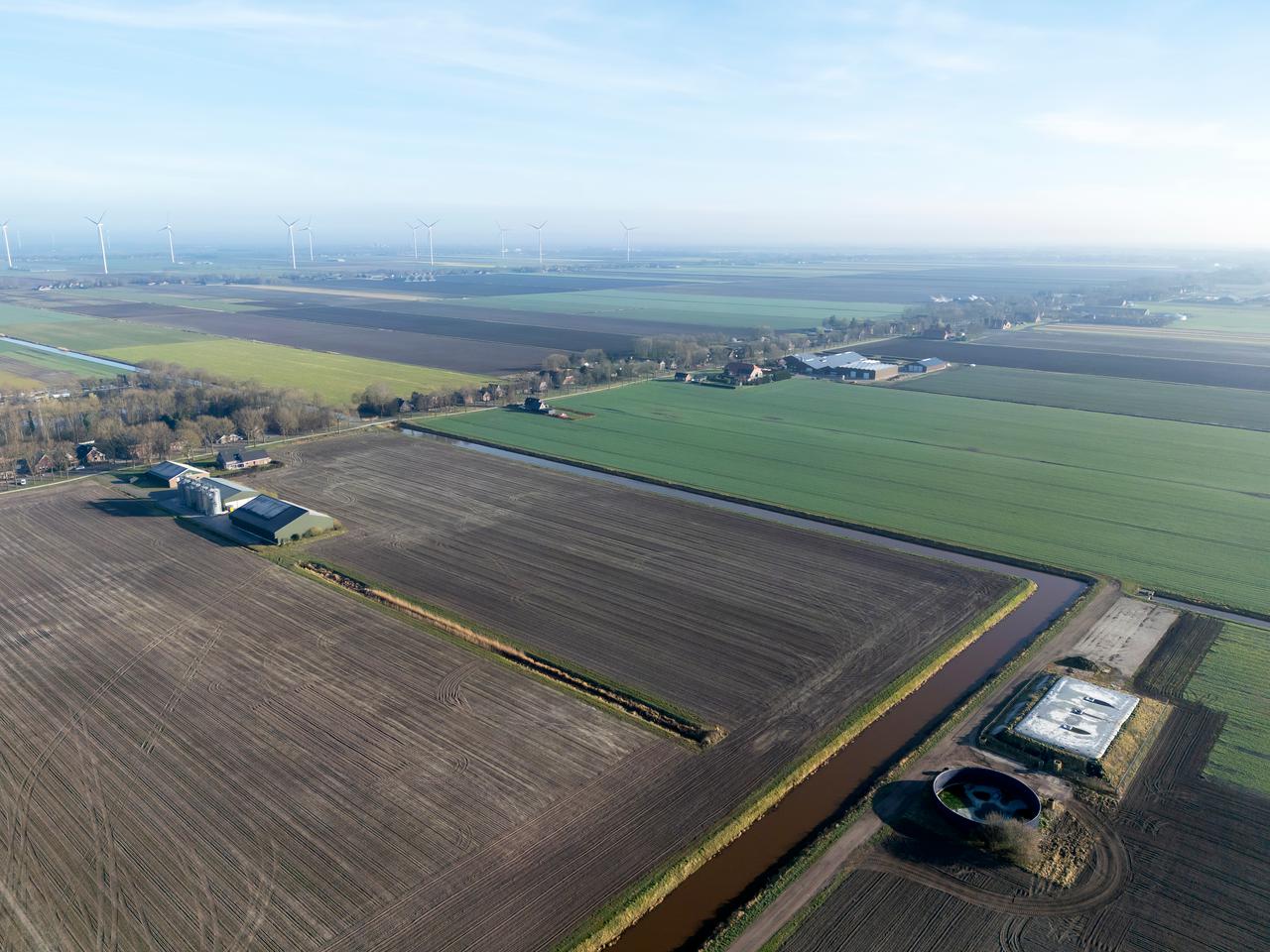 Dronefoto van Drenthe met akkers, grasland, boerderijen en windmolens op de achtergrond.