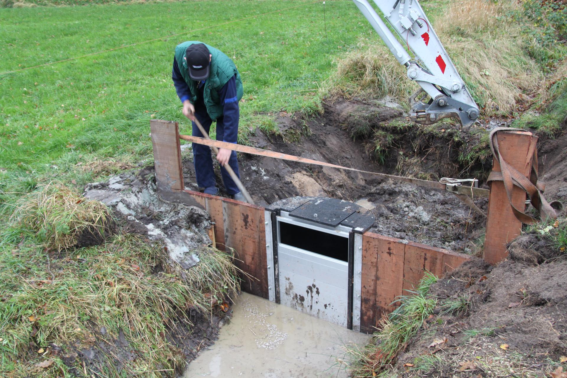 man legt stuw aan in sloot naast weiland
